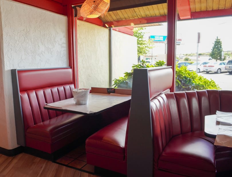 Red vinyl booths and tables with paper coverings inside a restaurant with large windows.
