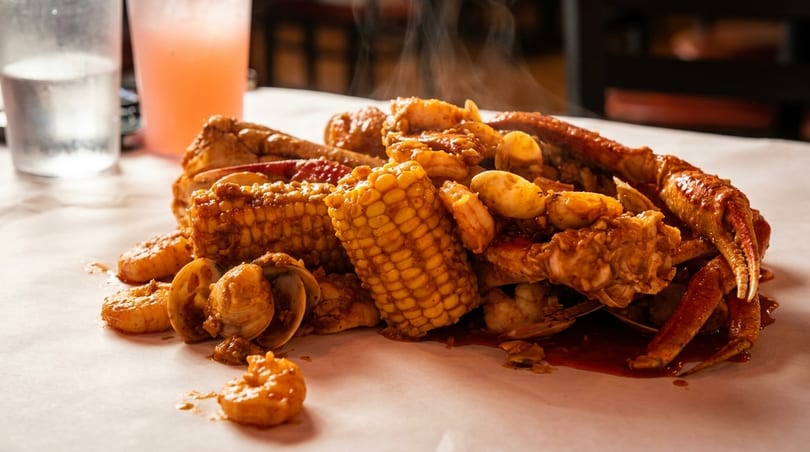 Steaming seafood boil with crab legs, shrimp, clams, and corn on the cob, on white paper.