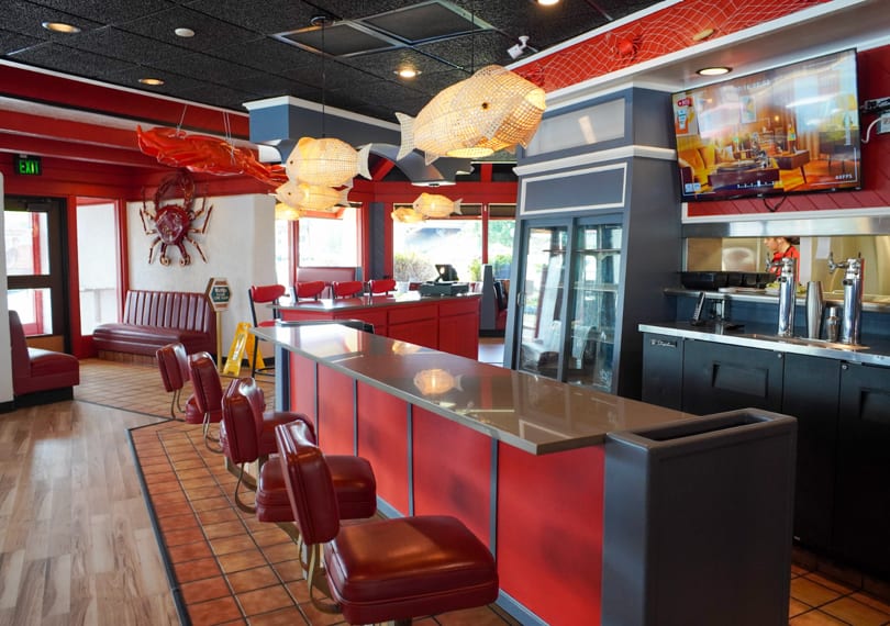 A vibrant red and black restaurant interior with a bar, booths, and fish-shaped light fixtures.
