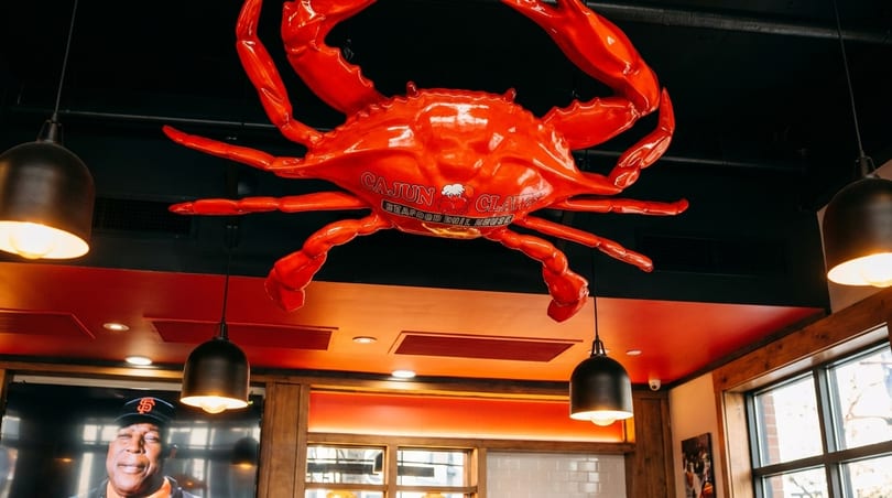 Large red crab sculpture with "Cajun Claws Seafood Boil House" text hanging from a black ceiling.