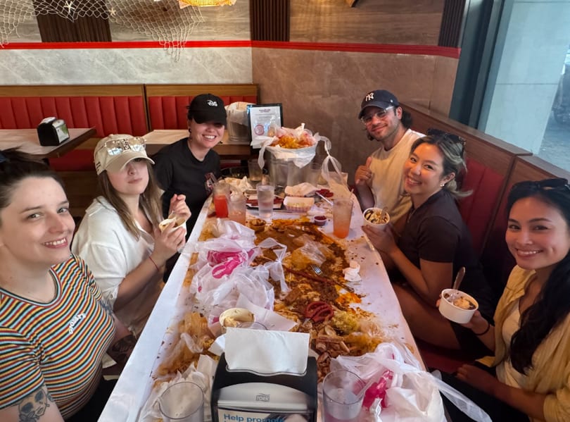 Six smiling friends gathered around a table covered in seafood boil remnants and drinks.