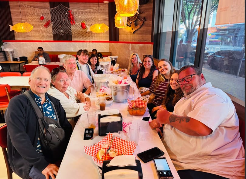 A large group of people smiling and sitting around a long table in a seafood restaurant.
