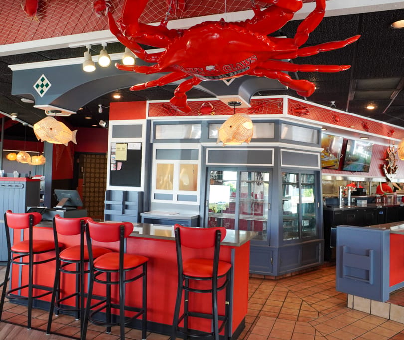 Restaurant interior with red bar stools, a large red crab decoration, and nautical-themed decor.