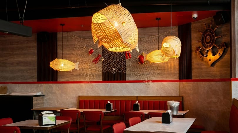 Restaurant interior with red booths, tables, and nautical decor including fish-shaped lights and a ship's wheel.
