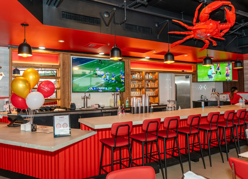 Vibrant red and black restaurant interior with a long bar, red stools, TVs, and a large crab decor.