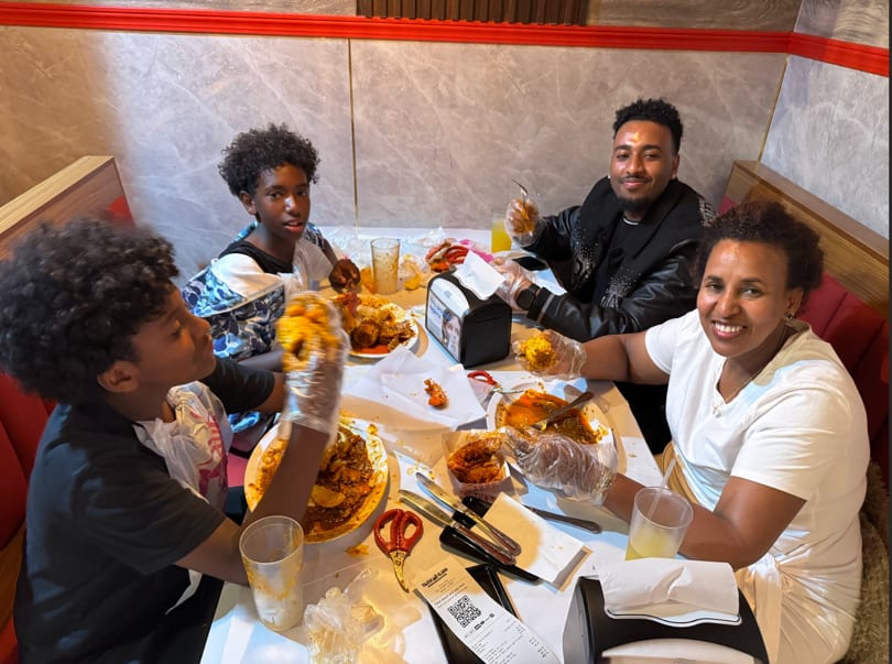 Four people, including two children, happily eating seafood with gloves at a restaurant table.