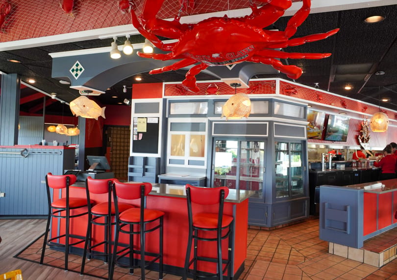Interior of a Cajun Claws restaurant with red bar stools, a large red crab decoration, and nautical decor.