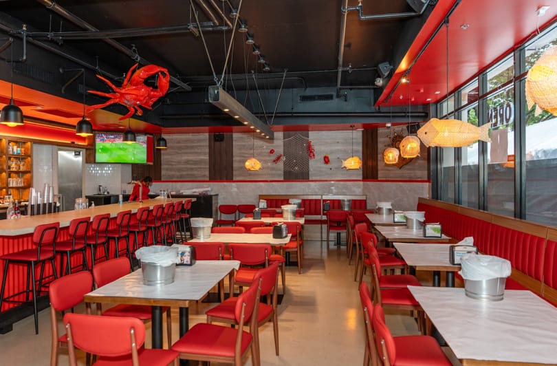 Spacious, empty restaurant interior with red chairs, white tables, a bar, and seafood-themed decor.