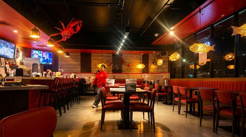 Restaurant interior with red decor, bar seating, dining tables, and a person walking.