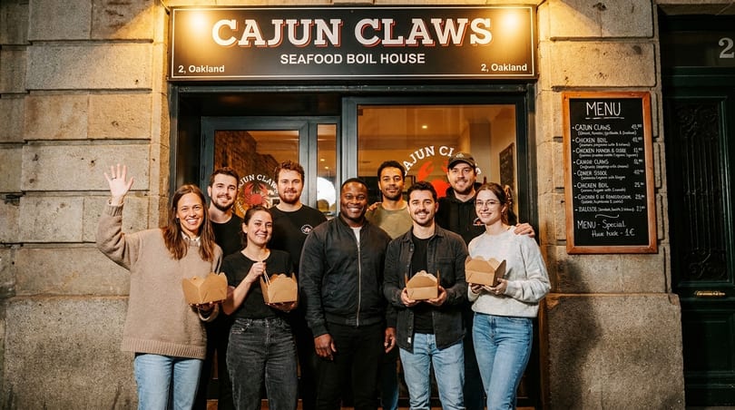 Eight smiling staff members stand outside Cajun Claws Seafood Boil House, holding takeout boxes.