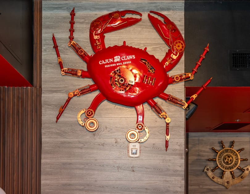 Large red crab art with gears and "Cajun Claws Seafood Boil House" text on a gray wall.
