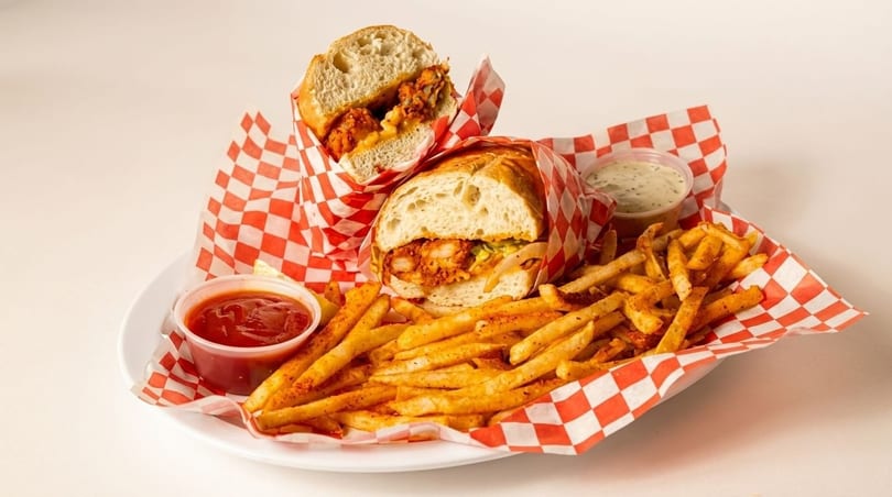 Two fried chicken sandwiches with fries, ketchup, and ranch dressing on a white plate.